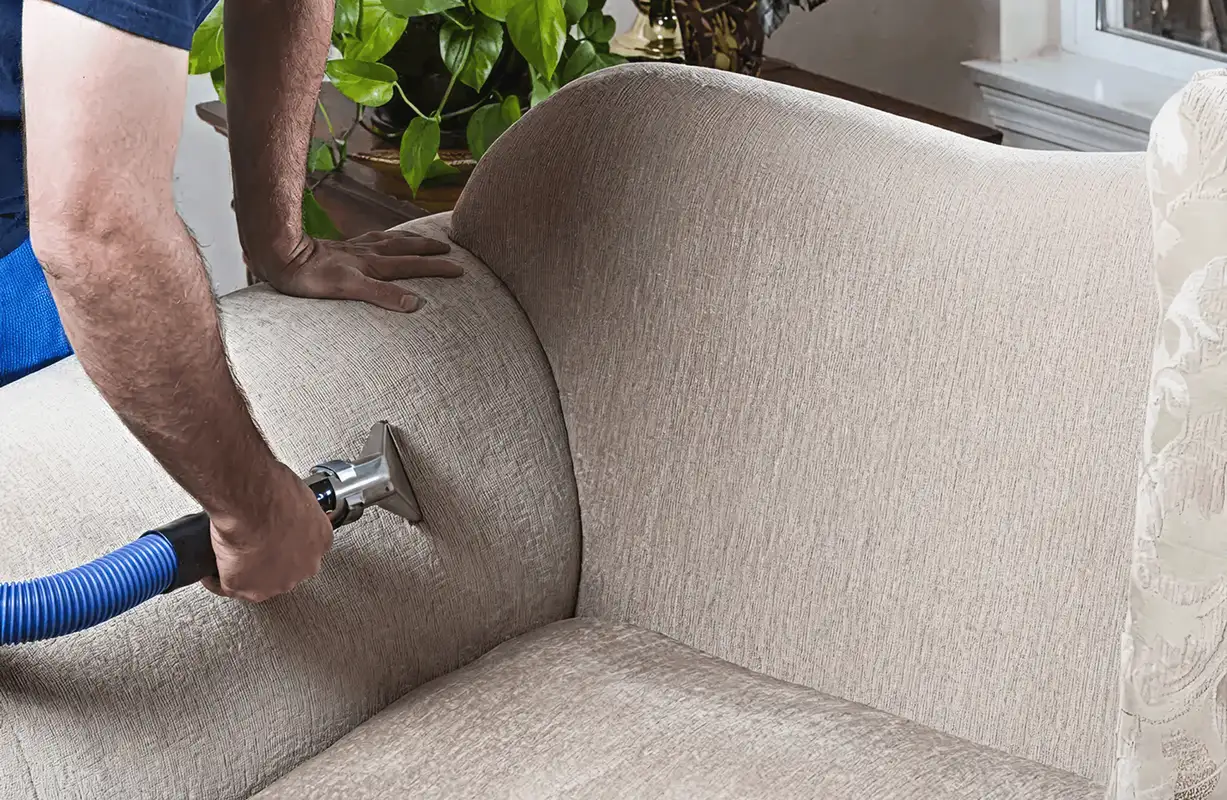 Professional upholstery cleaner deep-cleaning a fabric sofa with a handheld extraction tool and hose, Colorado Springs, CO.